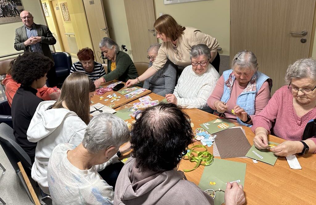 Seniorzy z DDS+ wraz z młodzieżą ze Szkoły Podstawowej w Sieniawie Żarskiej wykonują kartki wielkanocne przy stole