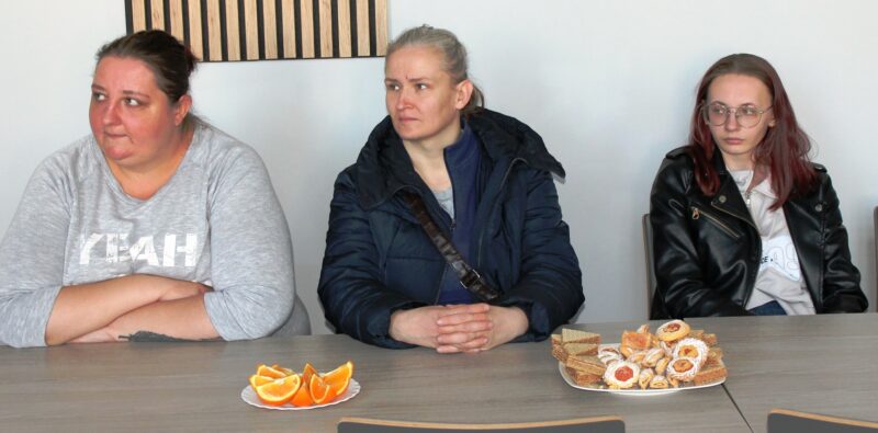 Na zdjęciu trzy uczestniczki siedzące przy stole, na którym stoją talerze z ciastkami i pomarańczami