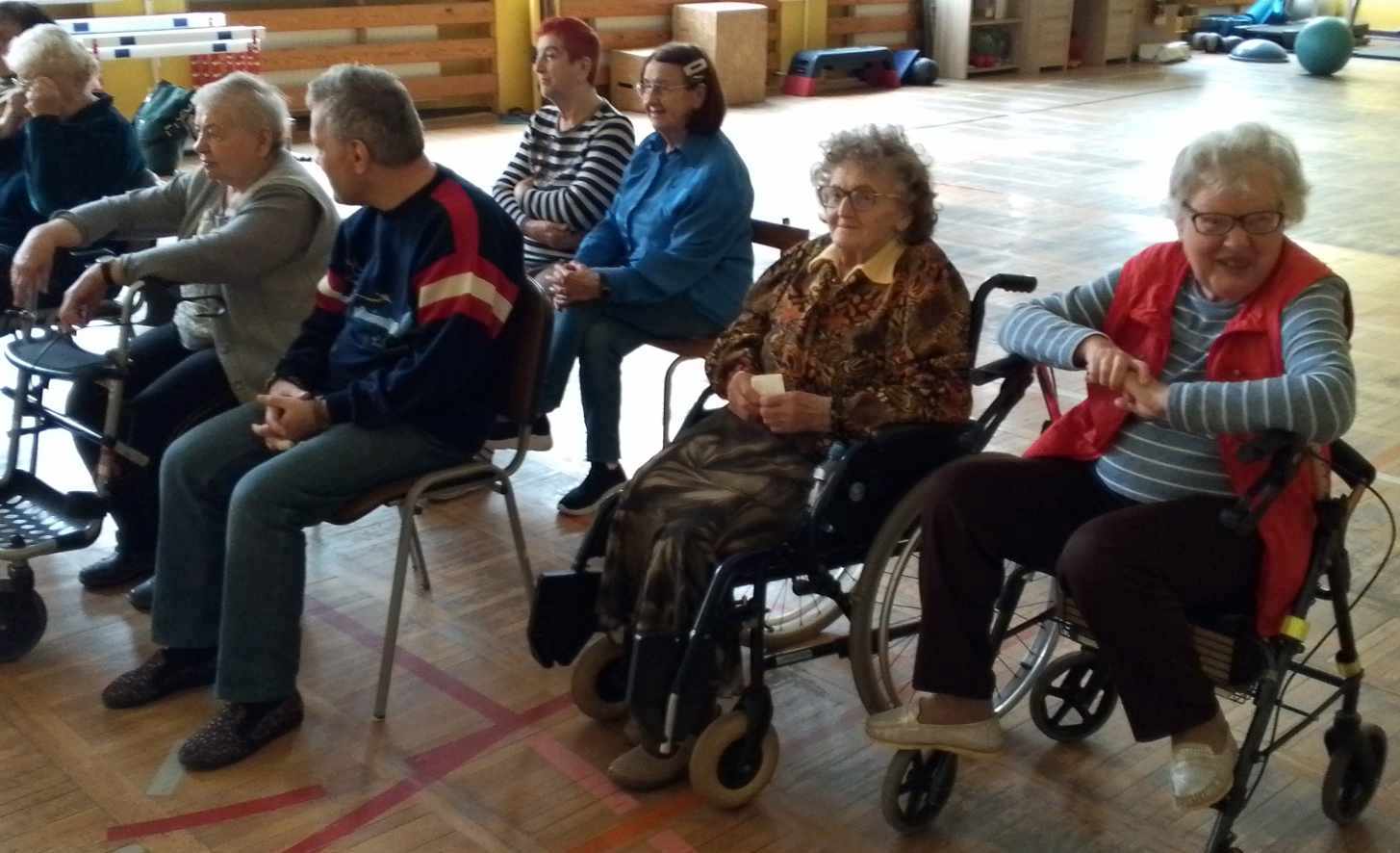 seniorzy siedzą w rzędach na sali gimnastycznej